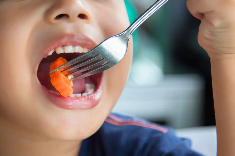 Anak makan wortel menggunakan garpu, close-up mulut terbuka