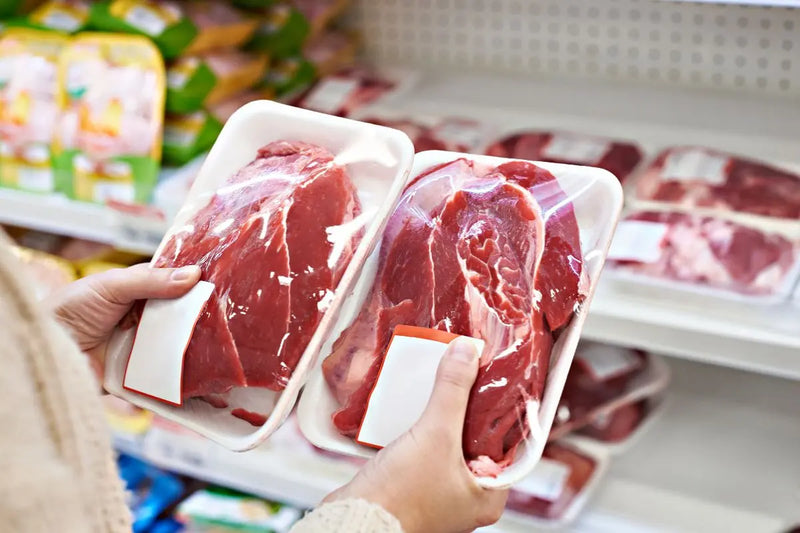Tangan membandingkan dua kemasan daging sapi segar di lorong supermarket