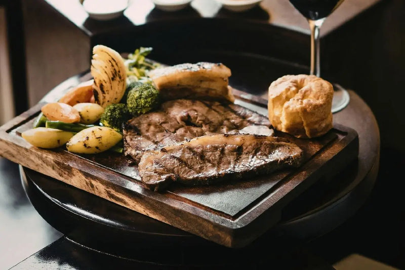 Sajian steak dengan kentang, brokoli, dan roti di atas talenan kayu