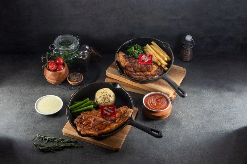 2 menu Steak Hotel by HOLYCOW! disajikan dengan kentang dan sayuran di wajan besi
