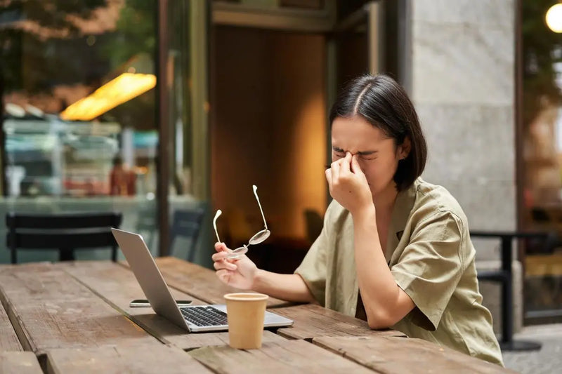 Wanita kelelahan memijat hidung di depan laptop