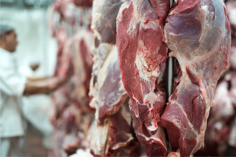 seorang pria berdiri di hadapan daging yang digantung