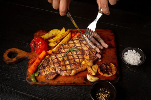 seseorang memotong daging steak dengan pisau dan garpu